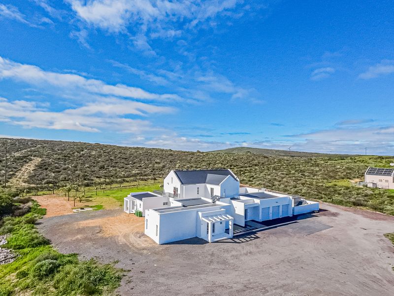 Aerial view of a modern white house with a pitched roof, multiple garage bays, and a pergola, situated in a spacious rural landscape.