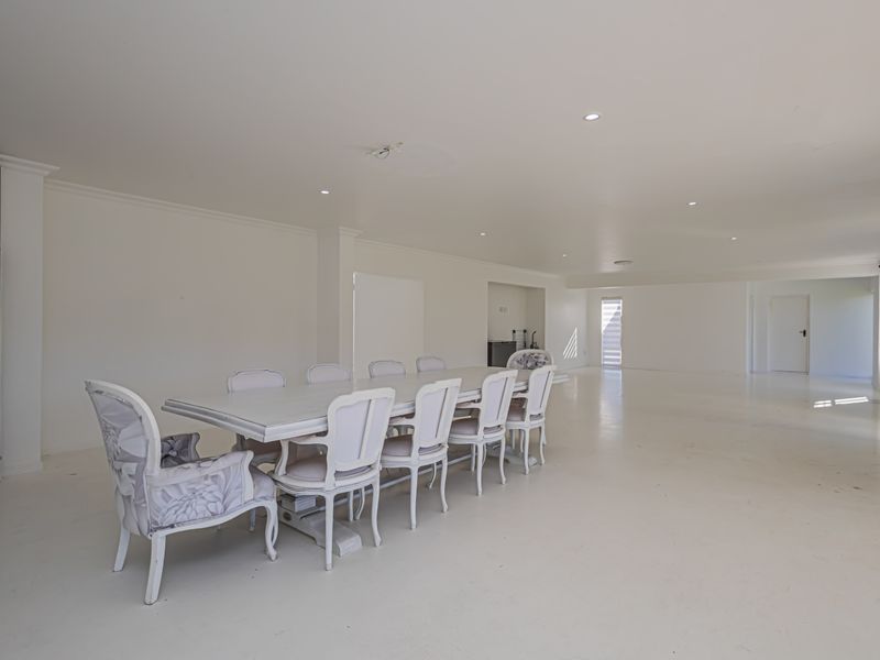 Spacious open-plan living and dining area featuring neutral white finishes, recessed downlighting, and a clean, minimalist aesthetic throughout the expansive floor space.