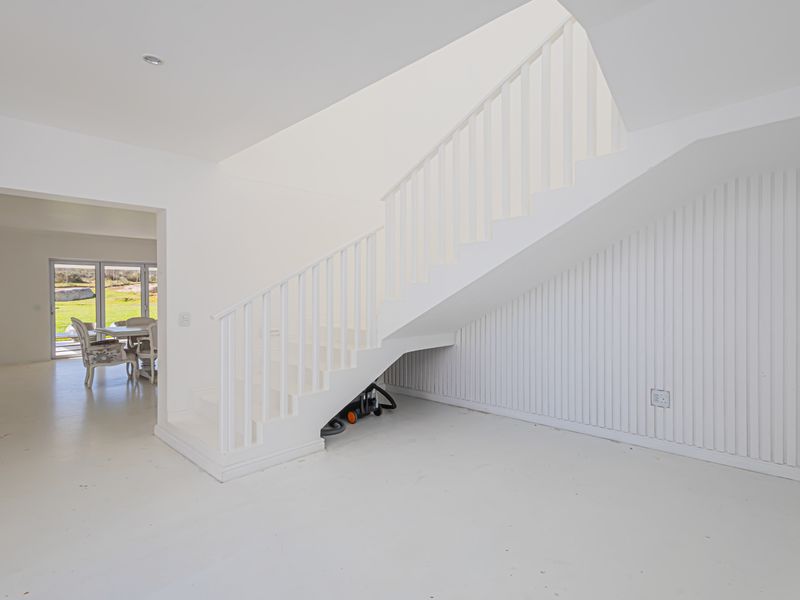 Bright, minimalist hallway featuring a white staircase with slatted wall paneling and clean, open transitions to adjacent living spaces.
