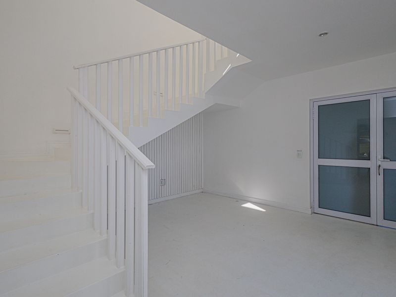 A bright, minimalist entrance area featuring a clean white staircase with a matching balustrade and a modern glass-paneled exterior door.