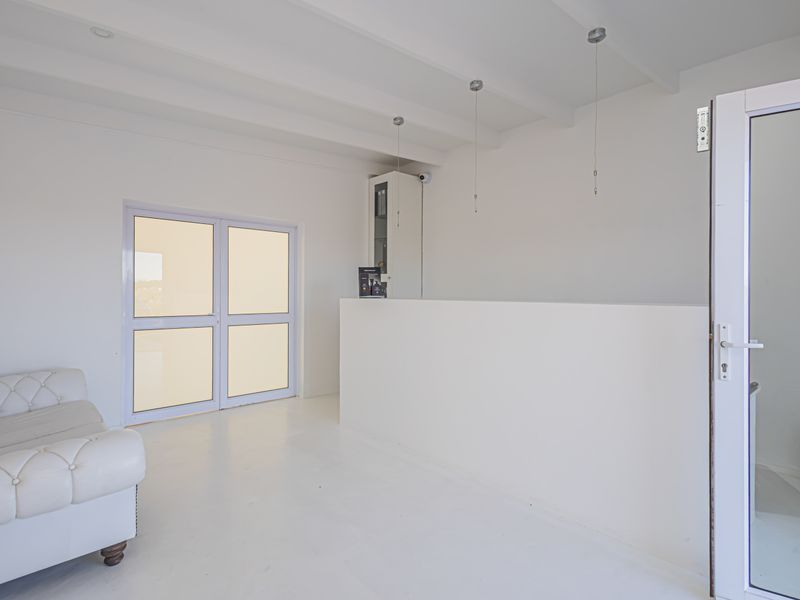 A bright, minimalist living area featuring exposed beam ceilings, a built-in counter, and glass double doors leading to an exterior space.