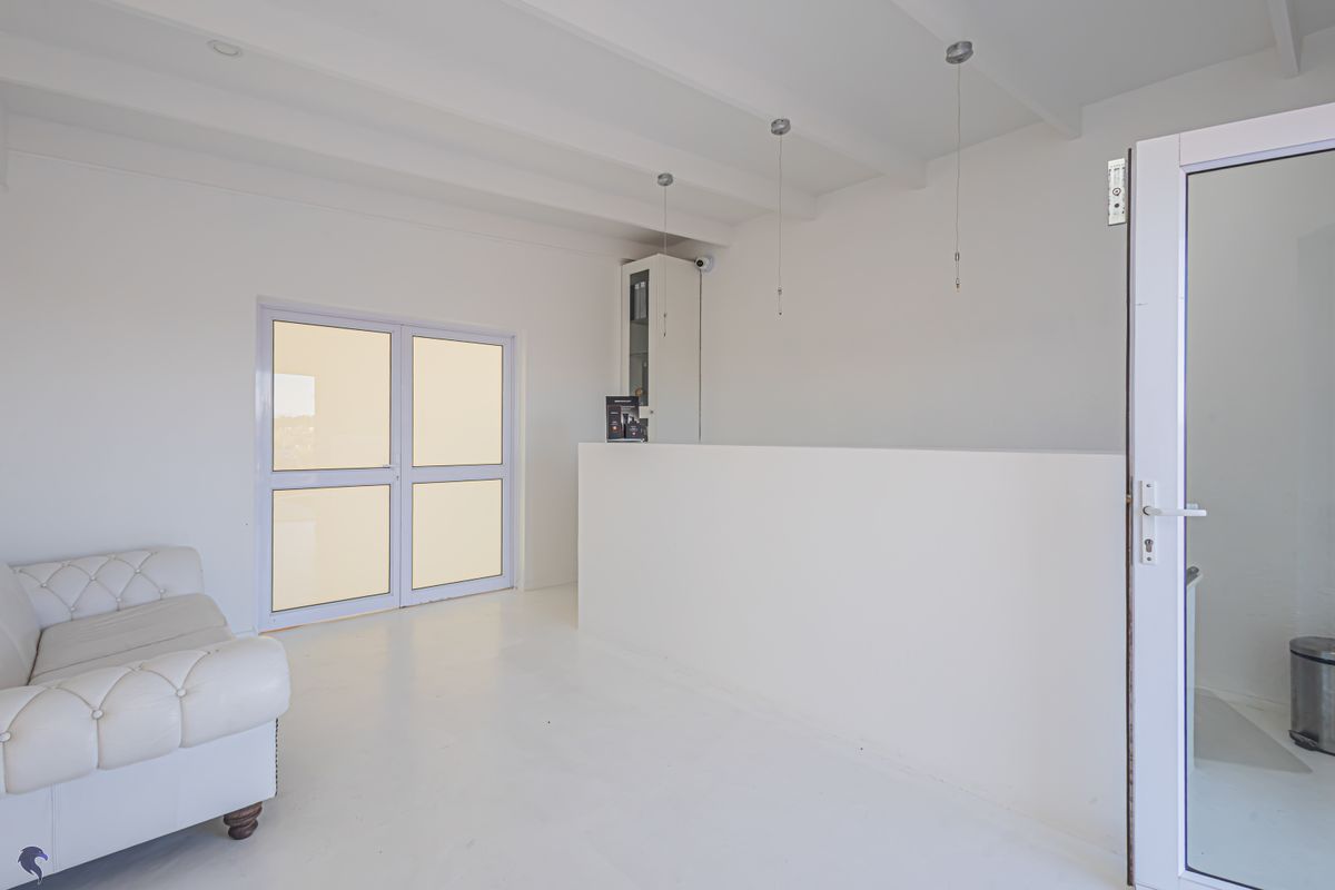 A bright, minimalist living area featuring exposed beam ceilings, a built-in counter, and glass double doors leading to an exterior space.