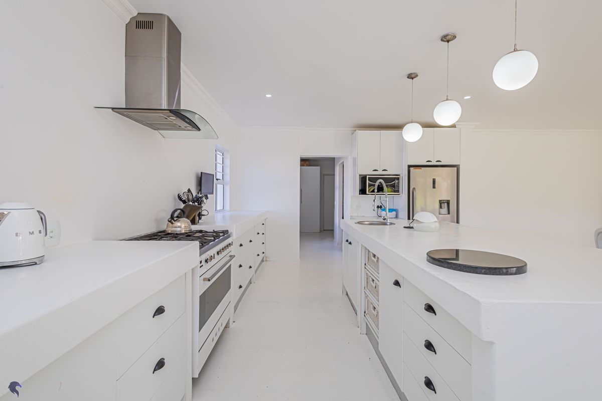 Modern white kitchen featuring a central island, gas stove with extractor, built-in oven, and ample cabinetry with sleek finishes.
