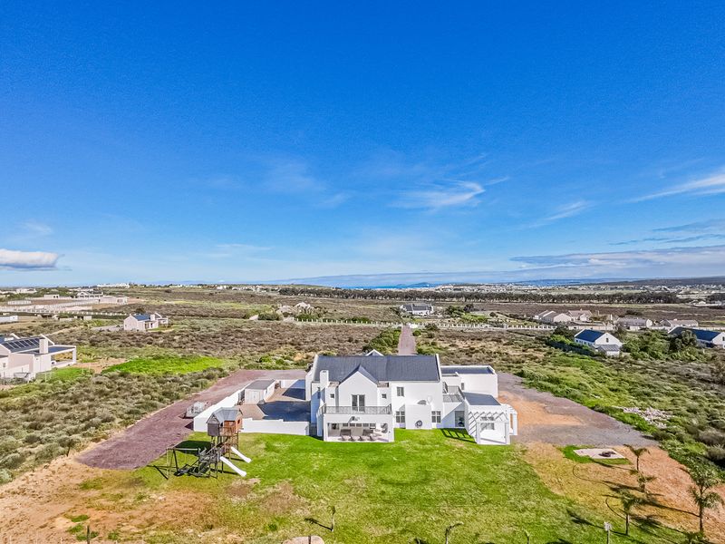 Aerial view of a large white residential property with a pitched roof, solar panels, and surrounding landscaped garden in a coastal estate setting.
