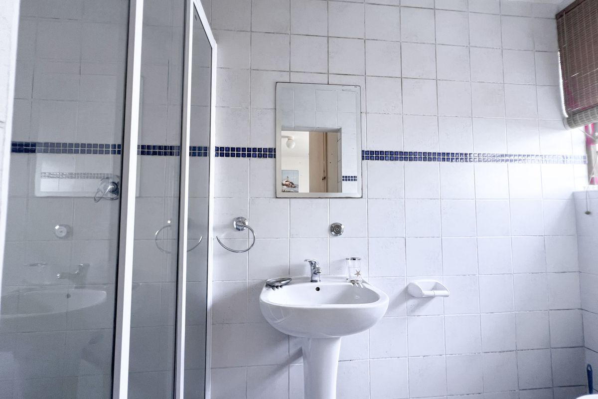 A functional bathroom featuring a pedestal basin, a glass-enclosed shower, and classic white wall tiling with a decorative blue accent border.