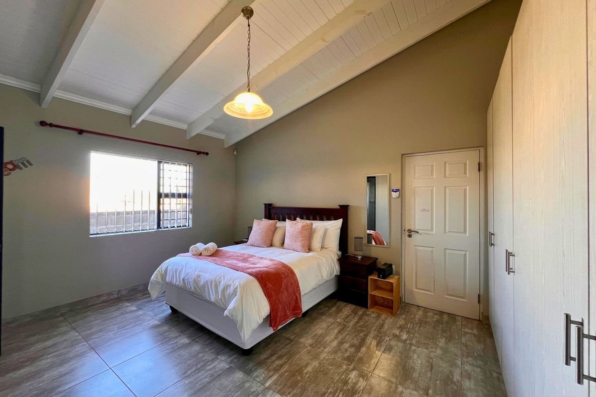 A well-maintained bedroom featuring vaulted ceilings with exposed beams, tiled flooring, and built-in cabinetry.