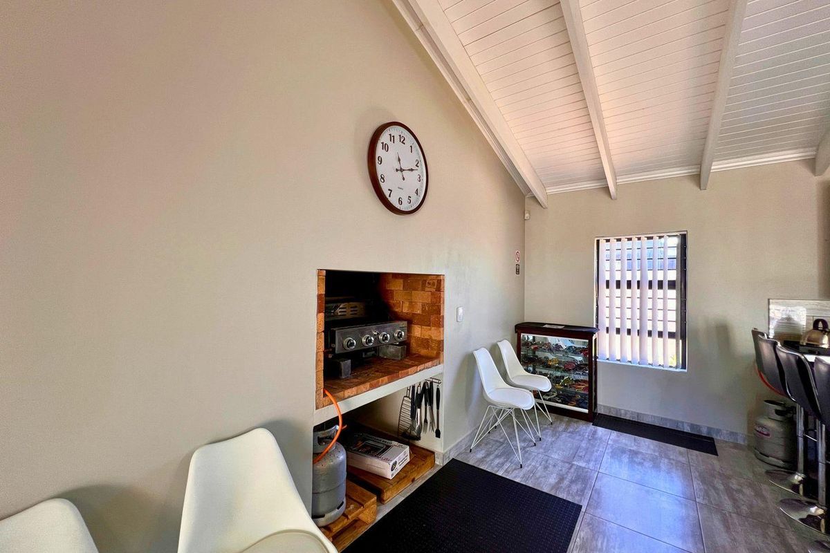 An indoor entertainment area featuring a built-in brick braai, tiled flooring, and a vaulted ceiling with exposed beams.