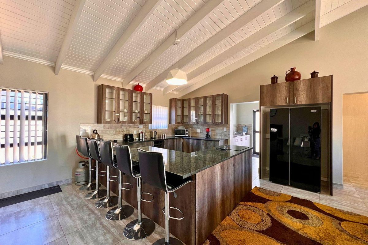 Spacious kitchen featuring a large granite-topped breakfast bar, wood-finish cabinetry, vaulted beamed ceilings, and tiled flooring, offering a functional and open layout.