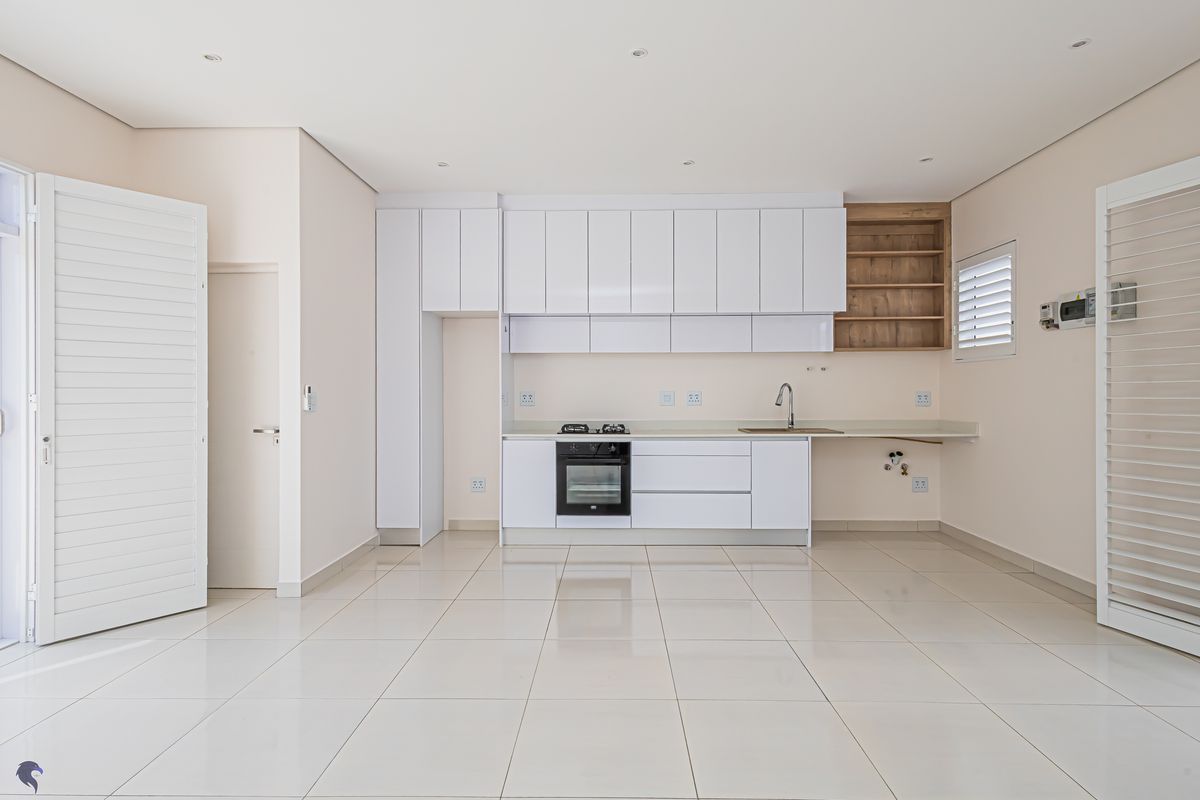 Modern open-plan kitchen featuring sleek white cabinetry, integrated oven, gas hob, and tiled flooring in a bright, spacious layout.