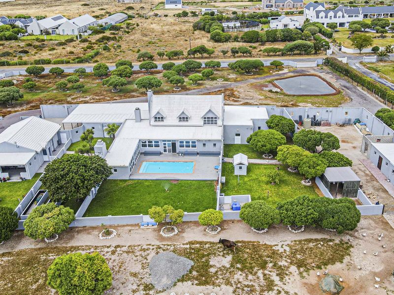 Aerial view of a large residential property featuring a central swimming pool, expansive lawn, multiple outbuildings, and a secure perimeter wall.