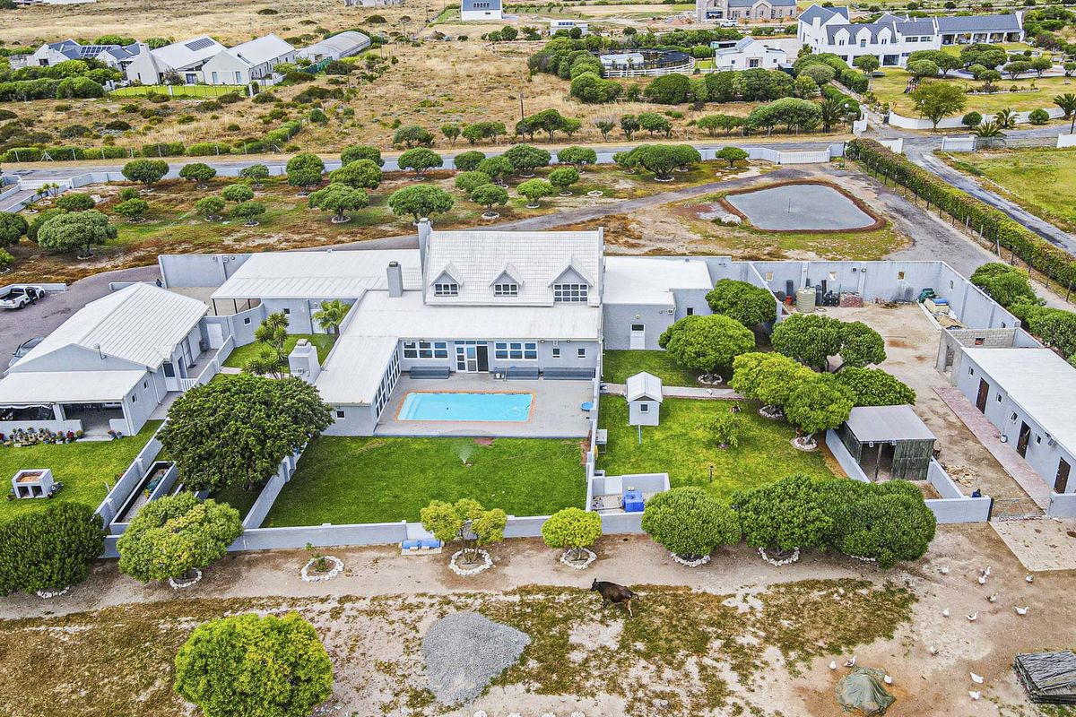 Aerial view of a large residential property featuring a central swimming pool, expansive lawn, multiple outbuildings, and a secure perimeter wall.