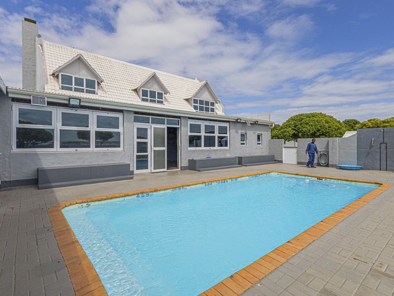 Outdoor pool area featuring a paved deck, swimming pool, and rear building elevation with white tiled roof and grey exterior walls.