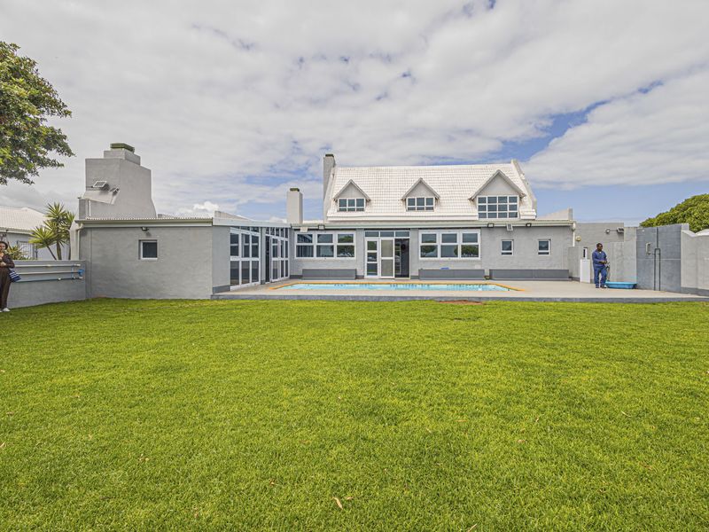 Rear view of the property featuring a spacious lawn, a swimming pool, and a paved patio area with a multi-level roof structure.