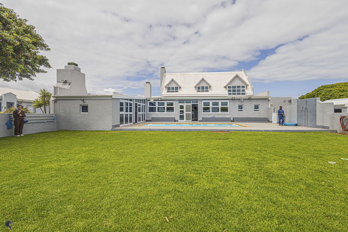 Rear view of the property featuring a spacious lawn, a swimming pool, and a paved patio area with a multi-level roof structure.