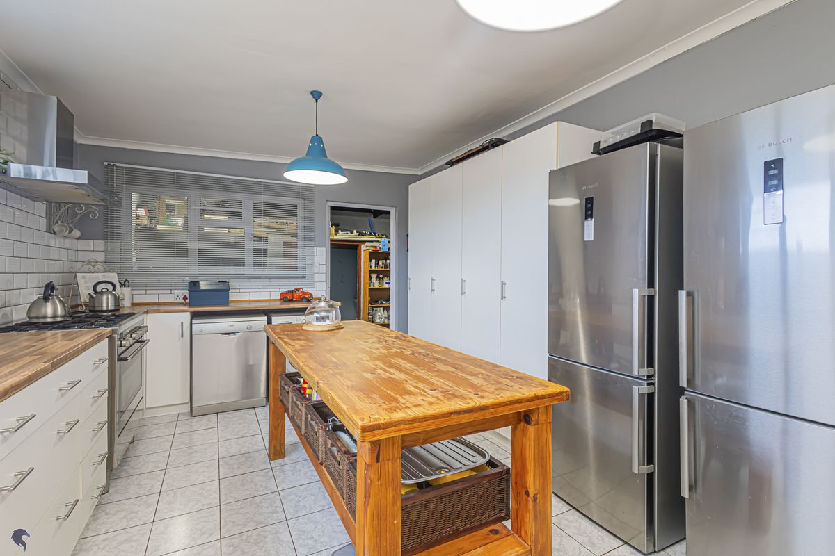A functional kitchen featuring white cabinetry, subway tile backsplash, stainless steel appliances, and a central wooden island, with an adjacent pantry area.