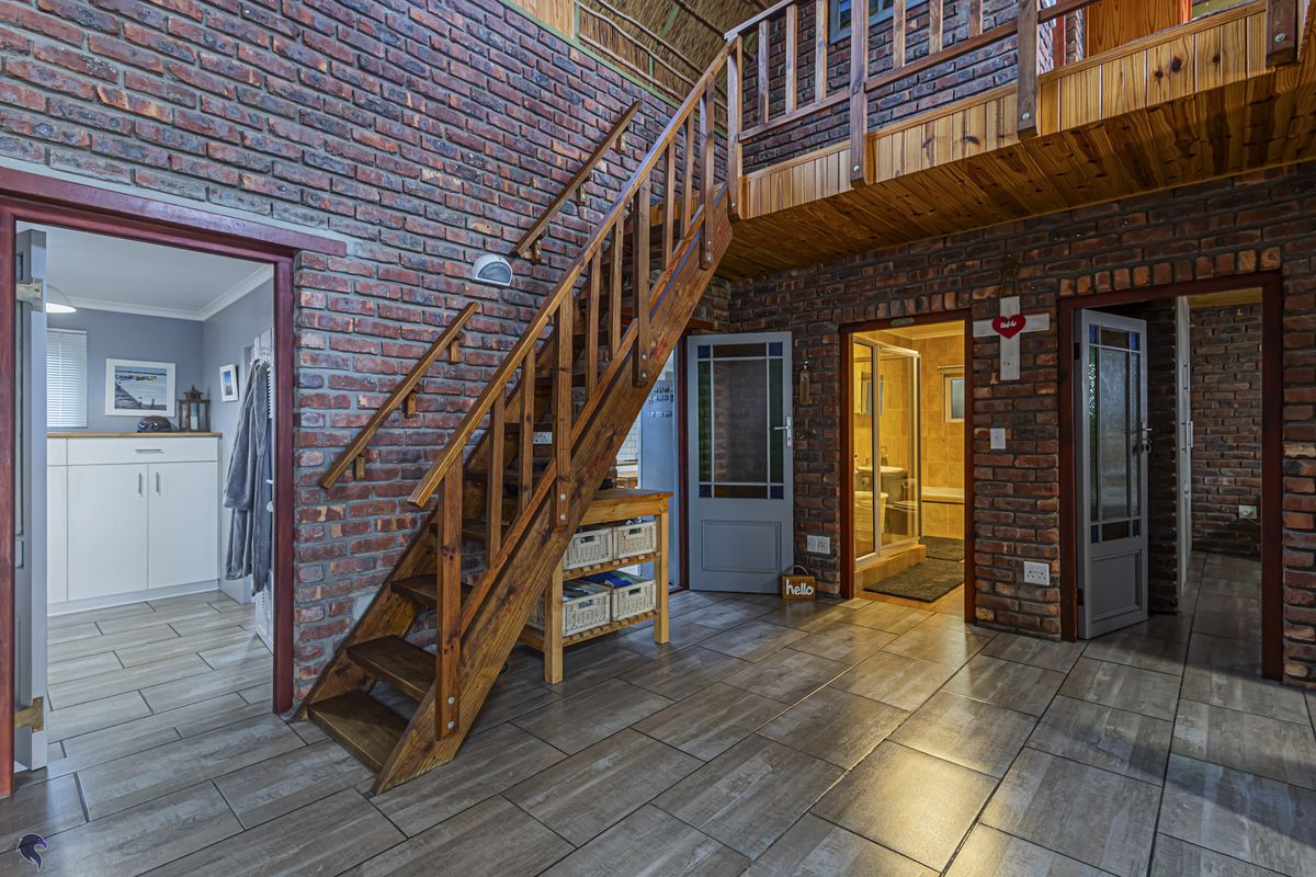 Spacious living area featuring rustic exposed brick walls, a timber staircase leading to a mezzanine level, and tiled flooring throughout.