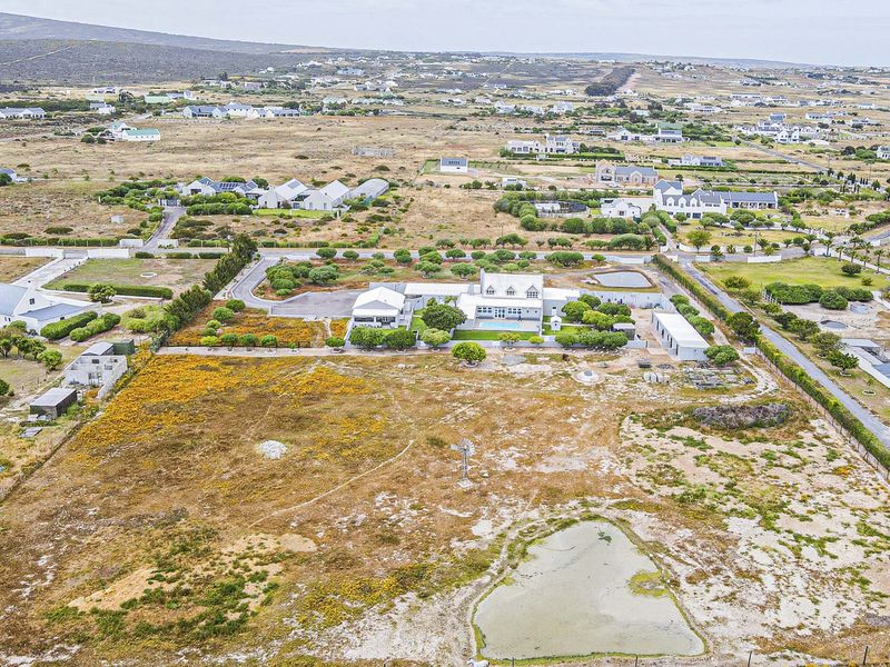 An aerial view of a large rural property featuring a main dwelling, a windmill, and a natural pond set within a spacious landscape.