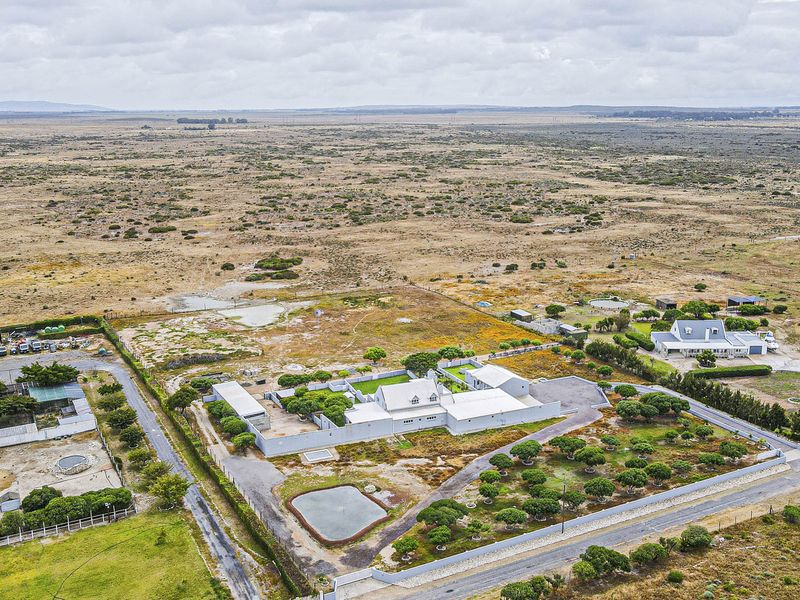 Aerial view of a large rural property featuring a main residence, outbuildings, paved driveway, and expansive surrounding grounds in a semi-arid landscape.