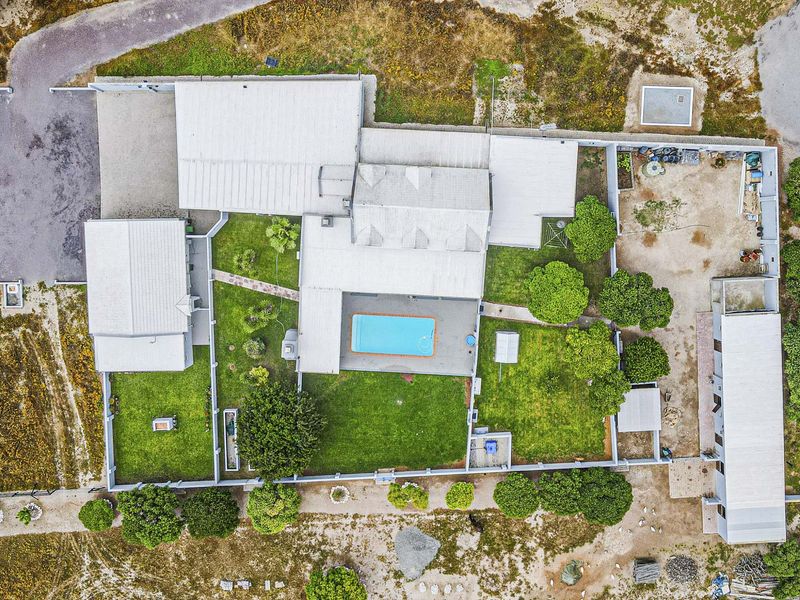 Aerial view of the property showcasing the main dwelling, swimming pool, surrounding garden, and driveway access.