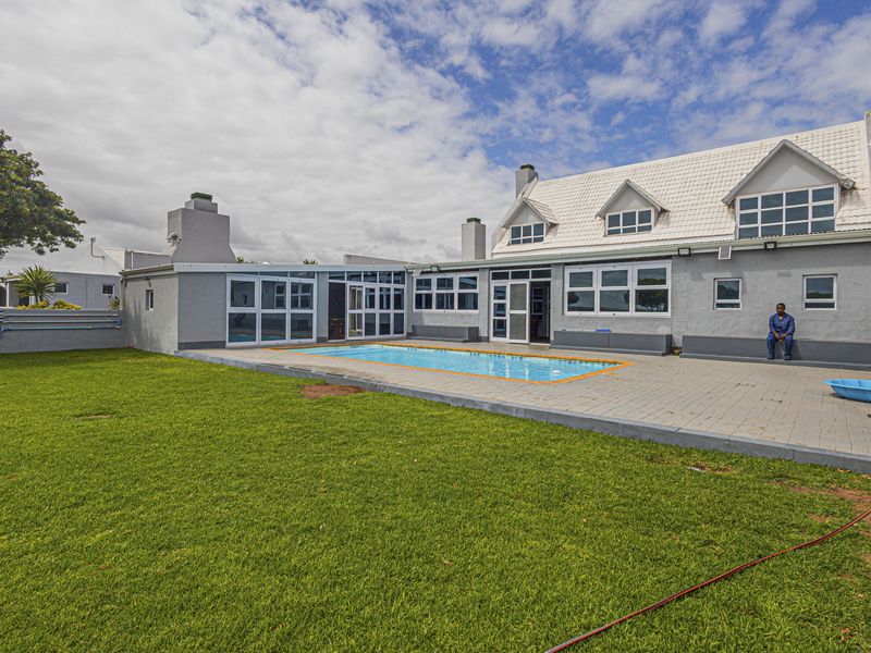 Rear exterior view of the house featuring a swimming pool, paved patio area, and a large lawn with a tiled roof structure.