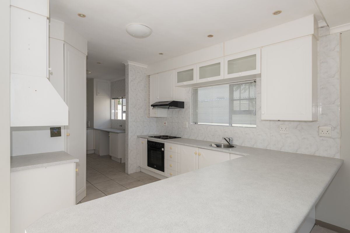 A functional kitchen featuring white cabinetry, a built-in oven and hob, and a breakfast bar, with an adjoining scullery area.