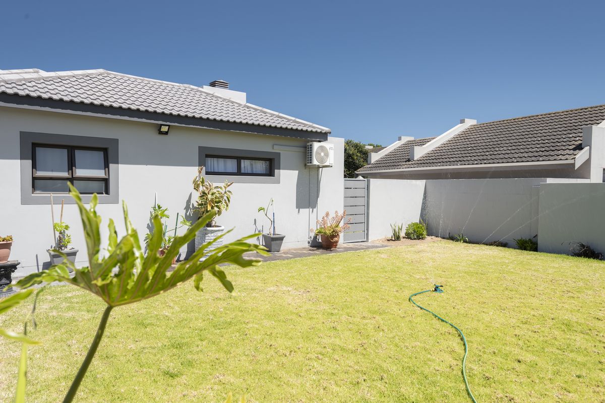A well-maintained rear garden featuring a manicured lawn, perimeter boundary walls, and an exterior wall-mounted air conditioning unit.