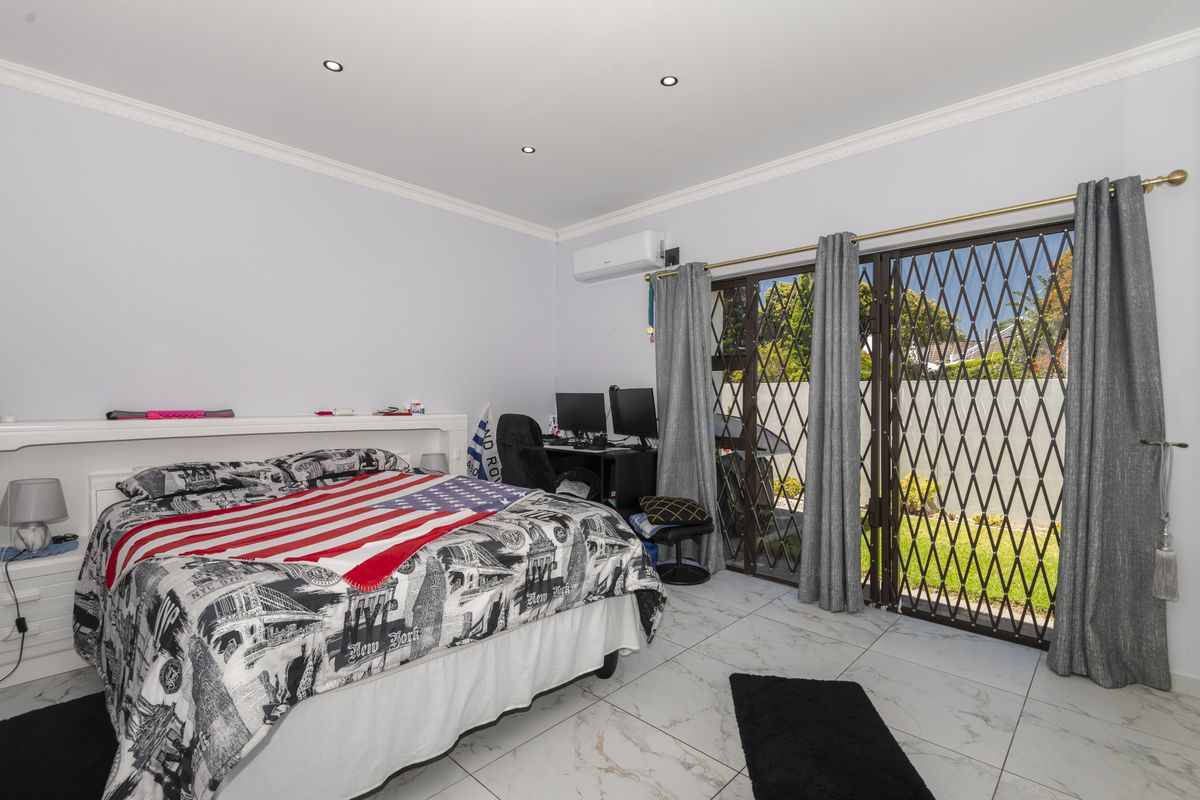 Spacious bedroom featuring tiled flooring, recessed ceiling lighting, a wall-mounted air conditioning unit, and sliding glass doors with security gates leading to the garden.