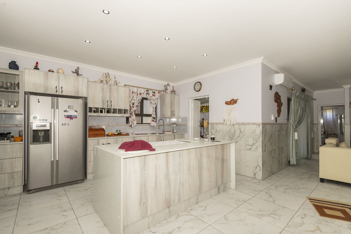 Modern kitchen featuring a central island, light wood-grain cabinetry, marble-style wall tiling, and recessed ceiling lighting.