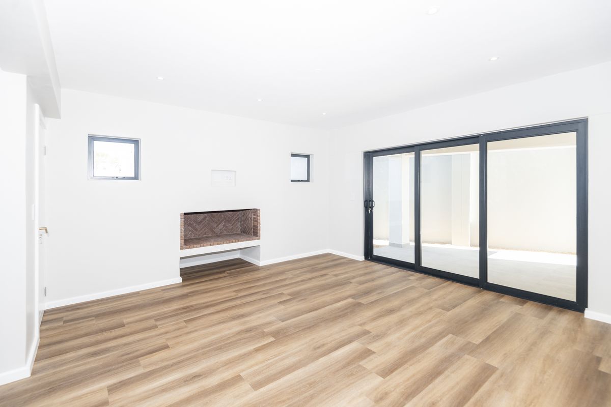 Bright and modern living room featuring wood-look flooring, a built-in brick fireplace, and large sliding glass doors leading to an outdoor area.