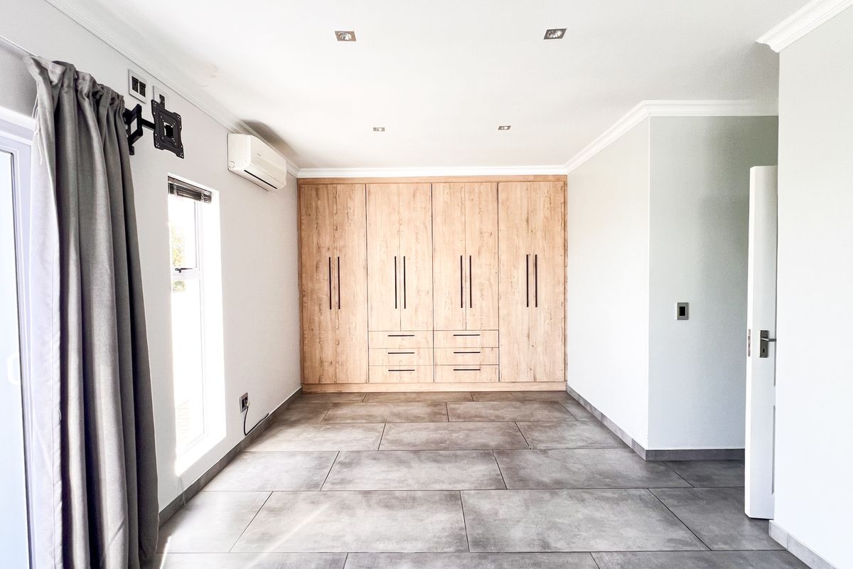 A bright bedroom featuring large format floor tiles, built-in wooden cabinetry, and a wall-mounted air conditioning unit.