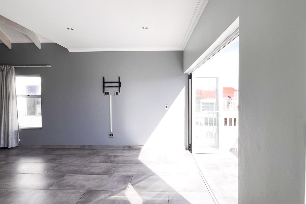 Spacious living area featuring large format floor tiles, recessed ceiling lighting, and wide sliding doors opening to an outdoor balcony.