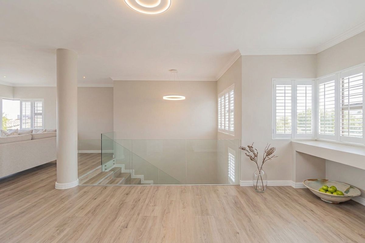 Spacious living area featuring modern glass balustrades, light wood-look flooring, and plantation shutters, creating a bright and contemporary open-plan atmosphere.