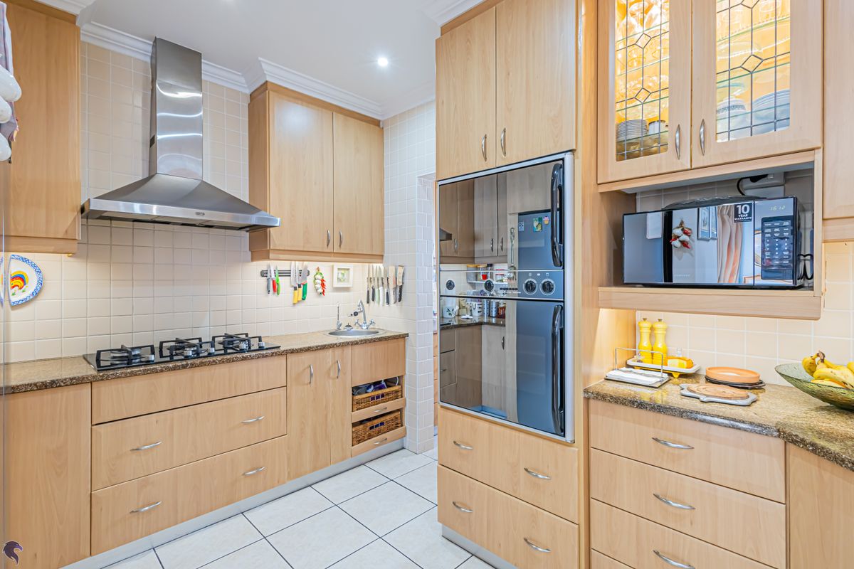 A well-maintained kitchen featuring light wood cabinetry, granite countertops, a gas hob with stainless steel extractor, and integrated oven unit.