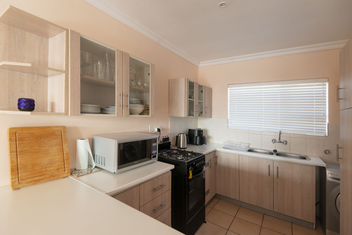 A functional kitchen featuring light wood-finish cabinetry, a double stainless steel sink, tiled splashbacks, and a freestanding gas stove.