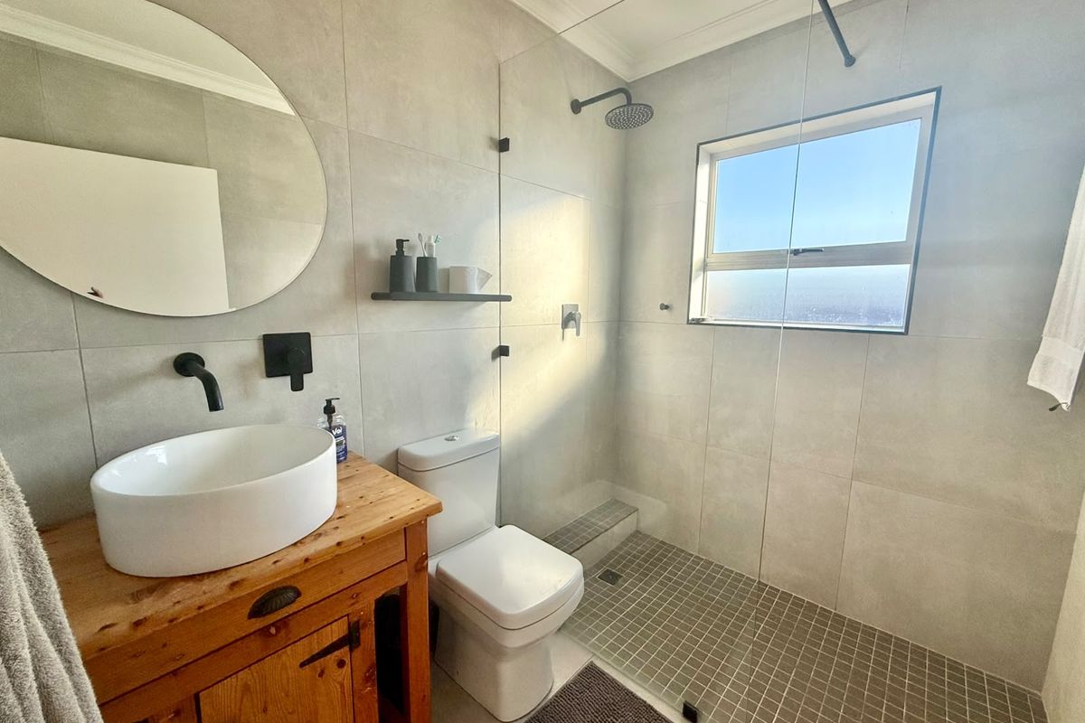 Modern bathroom featuring a walk-in shower with glass screen, wall-mounted matte black fixtures, a vessel sink on a wooden vanity, and large-format grey tiling.