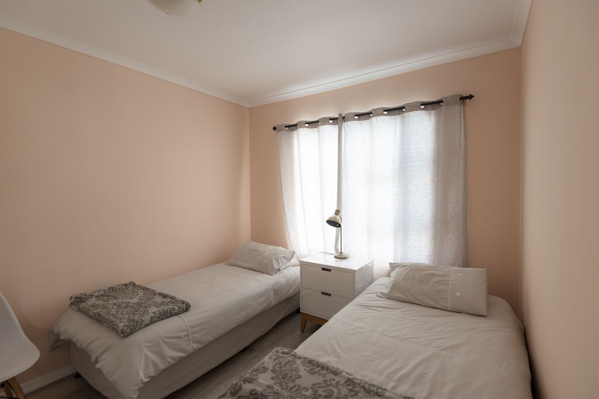 A well-lit bedroom featuring neutral wall tones, laminate flooring, and a large window with curtain fixtures.