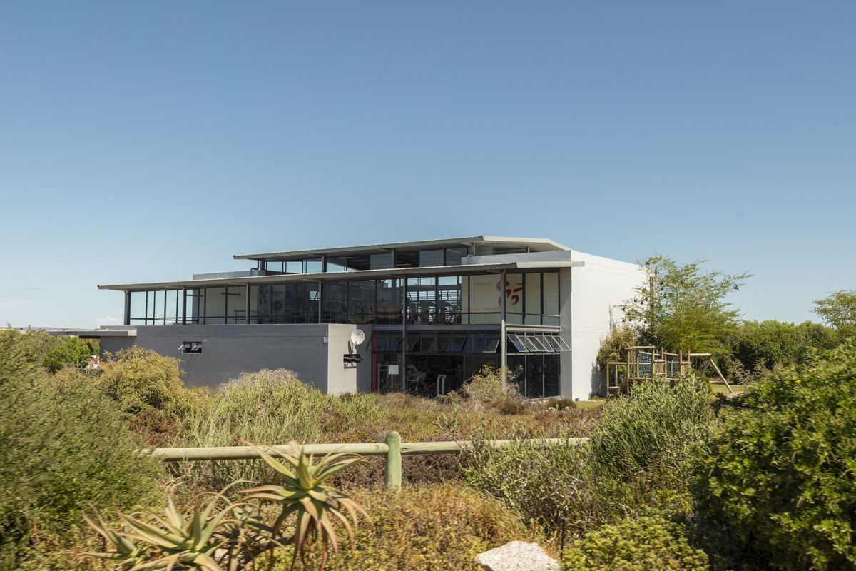 A modern multi-level residential building featuring expansive glass facades, a flat roof design, and integrated outdoor living spaces, set within a natural landscape.