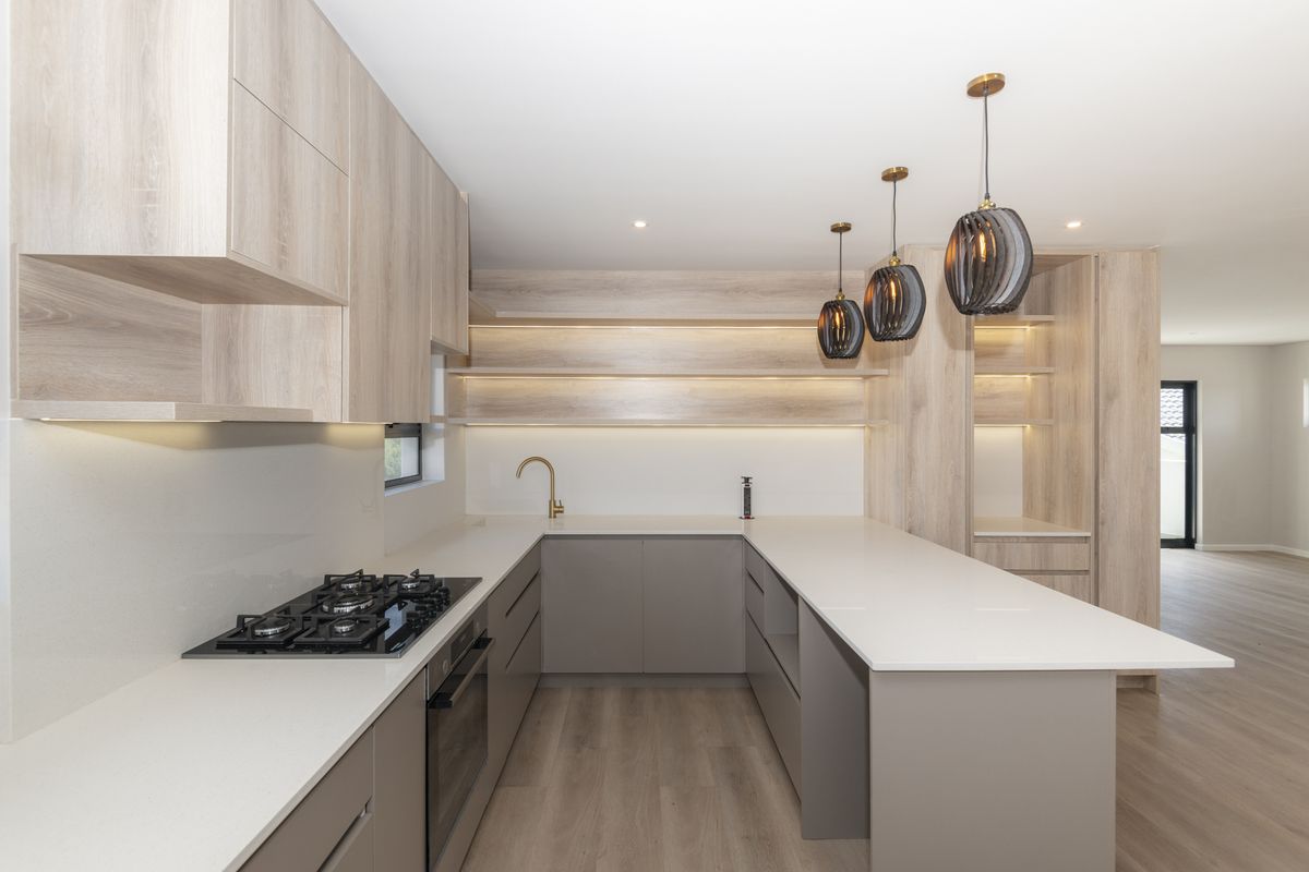 Modern kitchen featuring light wood cabinetry, stone countertops, integrated gas hob, built-in oven, and stylish pendant lighting over the breakfast bar.