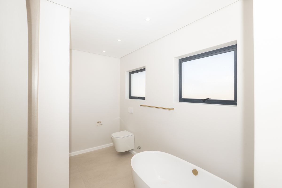 A modern, minimalist bathroom featuring a sleek freestanding bathtub, wall-mounted toilet, and contemporary fixtures with clean lines and neutral finishes.