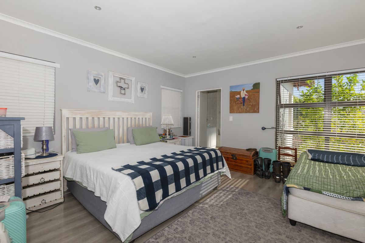 A well-lit bedroom featuring laminate flooring, recessed ceiling lighting, and large windows with fitted blinds, providing a comfortable and functional living space.