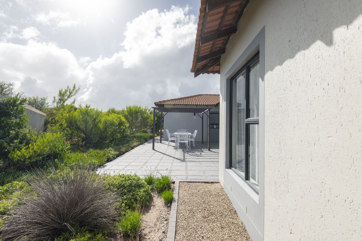 A well-maintained rear exterior view featuring a paved patio area, a pergola, and established garden landscaping alongside the house structure.