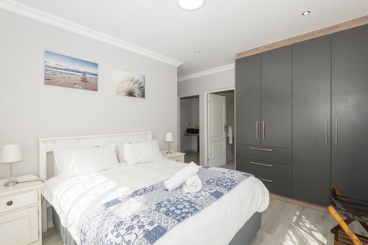 A well-maintained bedroom featuring built-in dark grey cabinetry, recessed ceiling lighting, and neutral flooring, with an adjoining en-suite bathroom.