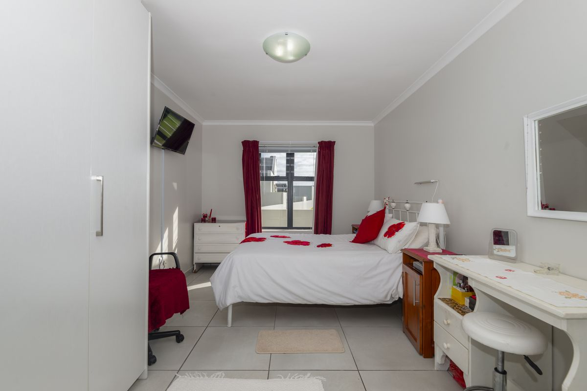 A functional bedroom featuring tiled flooring, built-in wardrobe, and a window with red curtains, providing a clean and simple living space.