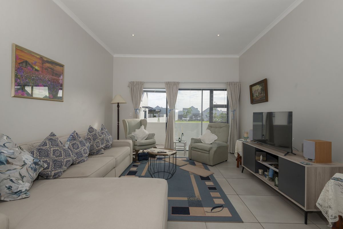 A well-maintained living room featuring neutral tiled flooring, recessed ceiling lighting, and large sliding glass doors providing access to an outdoor patio area.
