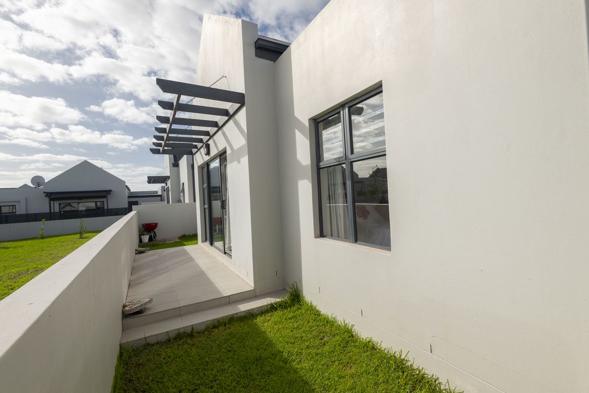 A modern exterior view of the property featuring a paved patio area, pergola structure, and well-maintained lawn.