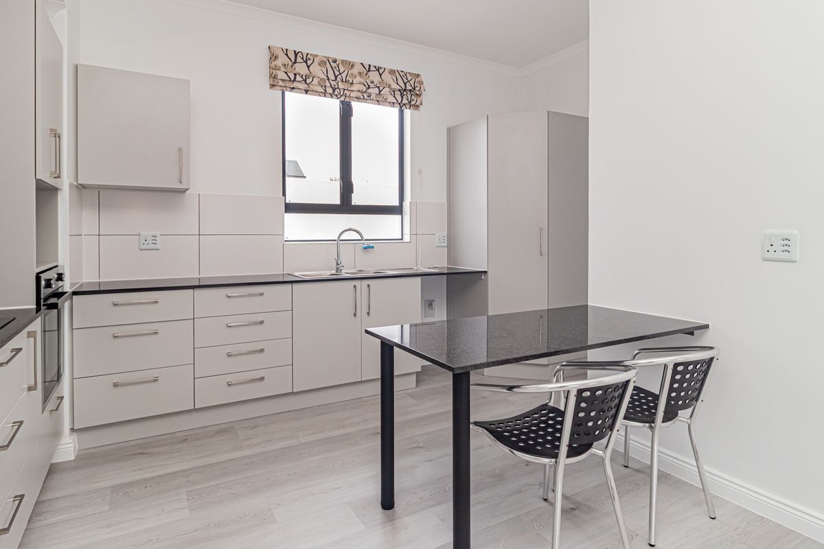 A modern, clean kitchen featuring light-toned cabinetry, dark granite countertops, a built-in oven, and a sleek stainless steel sink.