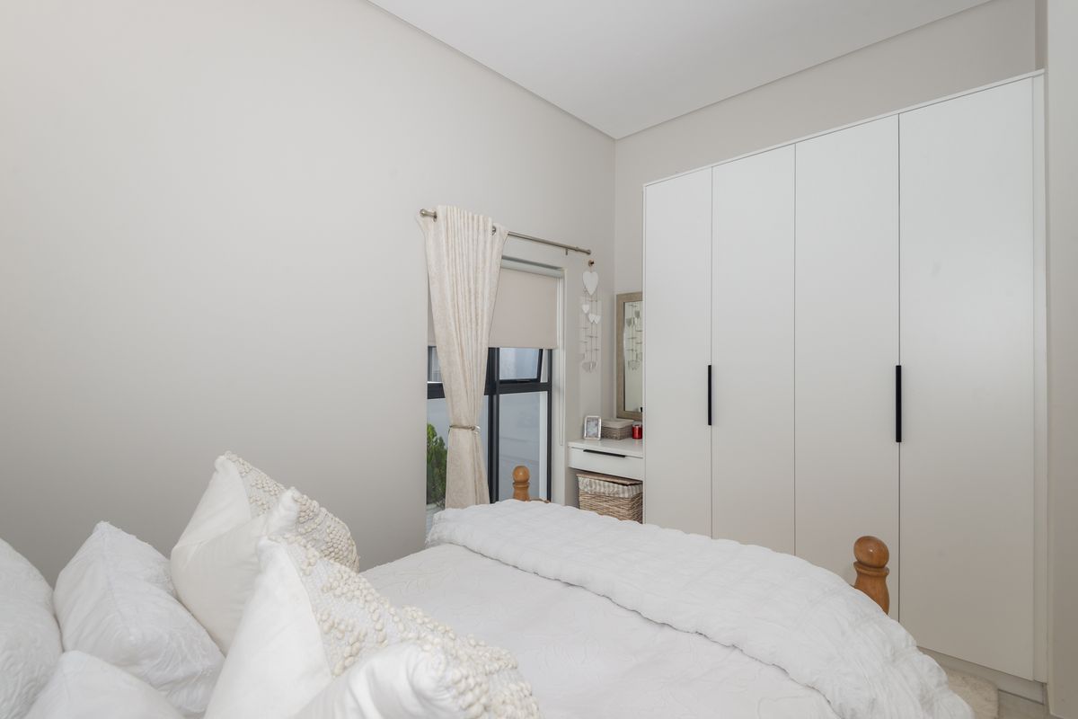 A bright bedroom featuring neutral walls, built-in floor-to-ceiling wardrobes, and a window with fitted blinds.