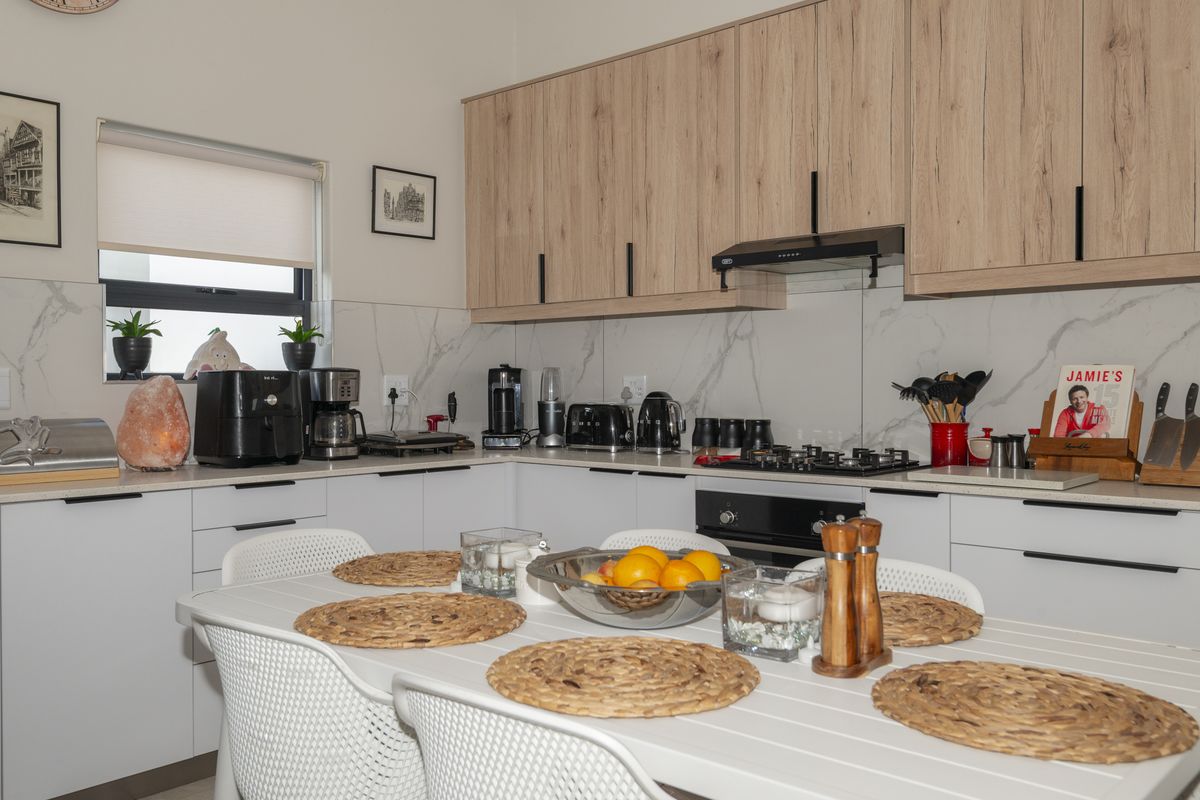 Modern kitchen featuring light wood-grain cabinetry, white stone countertops, marble-look splashback, built-in oven, gas hob, and integrated extractor fan.