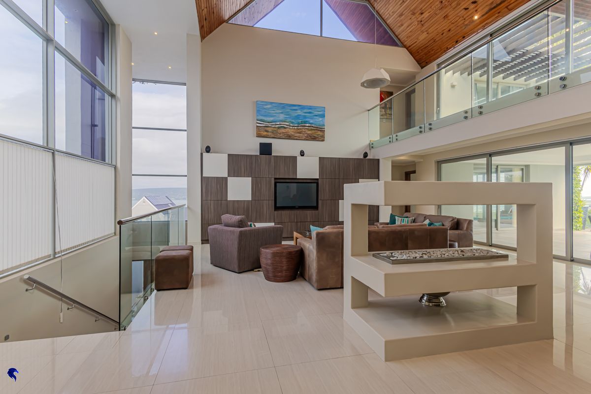Spacious double-volume living area featuring high timber ceilings, large glass windows, a modern built-in media unit, and a contemporary central gas fireplace.