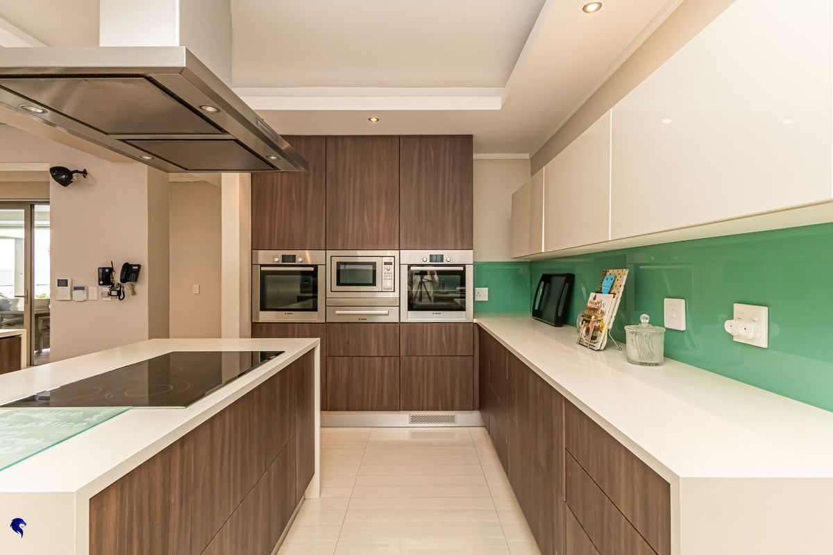 Modern kitchen featuring high-end integrated appliances, sleek wood-finish cabinetry, stone countertops, and a vibrant glass splashback with a central island cooktop.